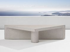 a concrete table sitting on top of a white floor next to a wall and ocean