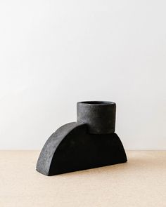 a black vase sitting on top of a table next to a white wall and floor