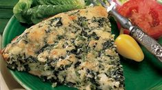 a green plate topped with spinach and tomato pie next to lettuce on a wooden table