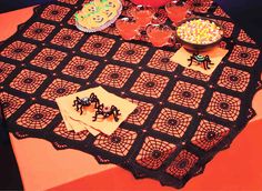 a table topped with cakes and drinks on top of a red table cloth covered in black doily