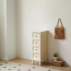 a white dresser sitting next to a wall with a basket hanging on it's side