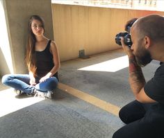 a woman sitting on the ground next to a man with a camera in front of her