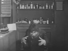 black and white photograph of a man sitting at a table in a room with lots of bottles on the wall