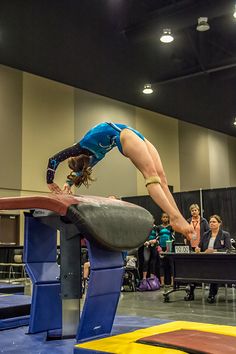 a woman doing a handstand on top of a trampoline in a gym