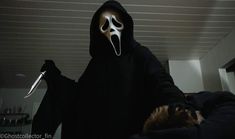 a person in a black hoodie with a white mask on holding a large knife