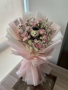 a bouquet of pink roses with a teddy bear in the center is sitting on a table