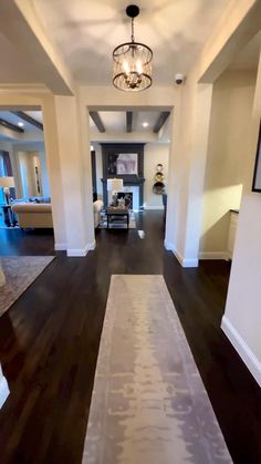 a hallway with hard wood flooring and white walls, along with a chandelier hanging from the ceiling