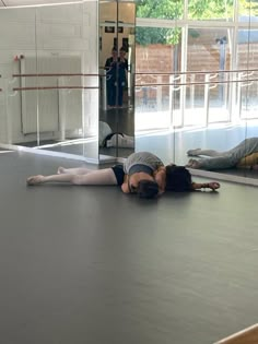 two people are laying on the floor in front of a mirror and one person is stretching