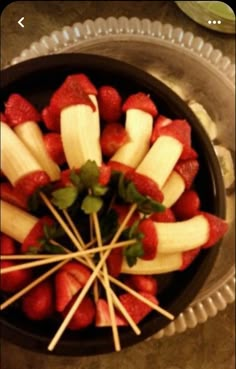 strawberries and apples arranged in a bowl on a table with toothpicks sticking out of them