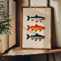 three fish are hanging on the wall next to a window with blinds and a potted plant