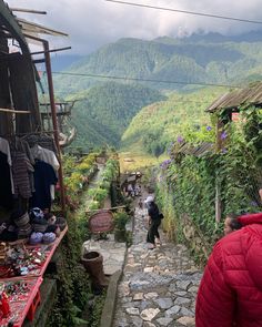 people are walking down the narrow cobblestone street with mountains in the backgroud