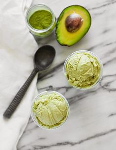 avocado ice cream in small cups next to an avocado and spoon