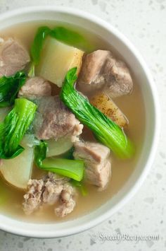 a white bowl filled with meat and vegetables on top of a marble countertop next to a cup of soup