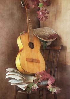 a guitar sitting on top of a wooden chair next to a hat and flower pot