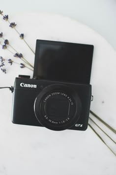 a black camera sitting on top of a table next to lavender flowers and a laptop