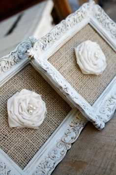 two white flowers are placed in an ornate frame on burlocked linens