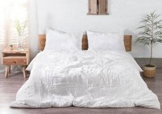 a bed with white sheets and pillows in a room next to a potted plant