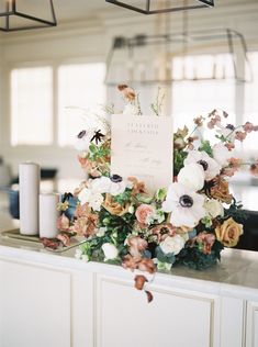 an arrangement of flowers and candles on top of a white counter in front of a window