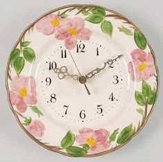 a clock with pink flowers painted on the front and sides, hanging from a wall