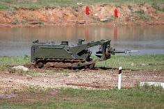 an army vehicle is parked in the mud near some water and dirt, while another vehicle sits on it's side