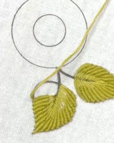 two yellow leaves on a white piece of fabric next to a circular stitching needle