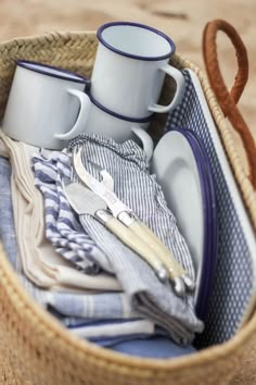 a basket filled with dishes and cups sitting on top of a beach