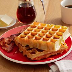 a plate with waffles and bacon on it next to a cup of coffee