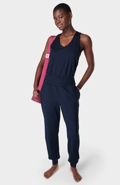 Perfect for low-impact studio workouts or just lounging around, this sporty jumpsuit is made from easy-moving stretch fabric with sweat-wicking properties. The relaxed fit is detailed with a keyhole racerback for added breathability. 60" length; 29" inseam; 10" leg opening (size Medium) Back keyhole with button-and-loop closure V-neck Sleeveless, with cutaway shoulders Front slant pockets Elastic waist Banded cuffs Moisture-wicking fabric engineered for dryness and comfort 85% polyester, 15% ela Womens Summer Jumpsuits, Long Pant Jumpsuit, Yoga Jumpsuit, Jumpsuit Navy Blue, Summer Jumpsuit, Jumpsuit Long, Yoga Outfits, Maternity Swimwear, Sweaty Betty