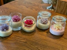 small jars filled with flowers on top of a wooden table covered in wax and candles