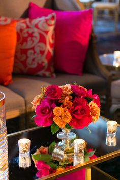 a glass table with flowers and candles on it in front of a couch, coffee table