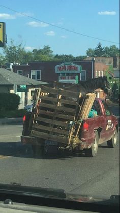 a red truck driving down a street next to a tall wooden structure on the back of it's flat bed