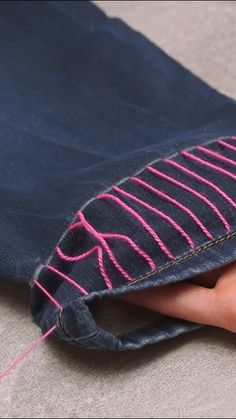 someone is stitching pink thread on the inside of a pair of blue denim jeans