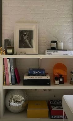 a book shelf with books and other items on it in front of a white brick wall