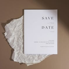 a white save the date card sitting on top of a piece of paper with torn edges