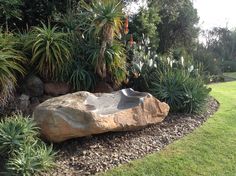 a large rock in the middle of a garden with plants around it and a bowl shaped like a birdbath