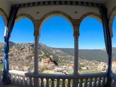 an ornate balcony with arches and blue curtains overlooks the city below in the distance