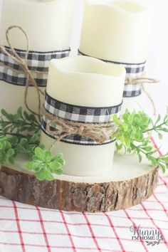 three white candles sitting on top of a piece of wood next to some green plants