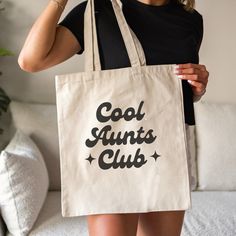 a woman holding a tote bag with the words cool aunts club on it