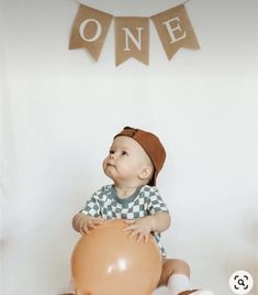 a baby sitting on the floor with a balloon in front of him and one banner above it