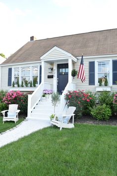 a white house with blue shutters and flowers on the front lawn in front of it