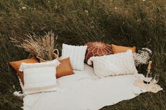 a blanket with pillows and vases on it in the middle of some tall grass