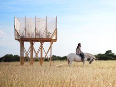 a woman riding on the back of a white horse next to a tall wooden structure