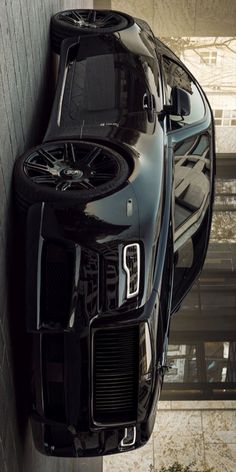 the front end of a black sports car parked on top of a brick wall next to a building