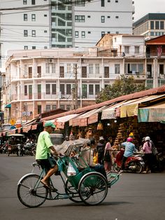 a man riding a bike down the middle of a street with lots of buildings in the background