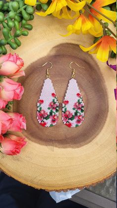 a pair of white and red earrings sitting on top of a wooden table next to flowers