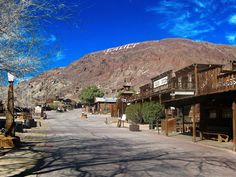 an old western town in the desert with mountains in the backgrouds and blue skies