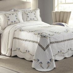 a white bedspread with blue flowers on it and a chair in the background