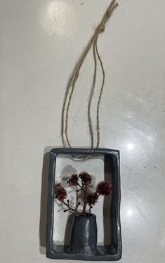 a vase with some flowers in it hanging from a string on a wall ornament