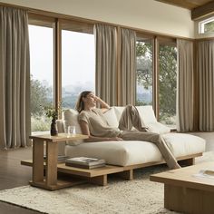 a woman laying on a white couch in front of large windows