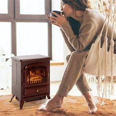 a woman sitting on the floor next to an electric stove holding a cup and looking at it